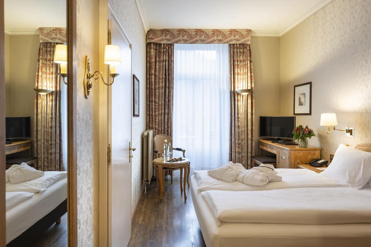 Ett hotellrum med två sängar, ett skrivbord, en stol, en TV och en lampa.
