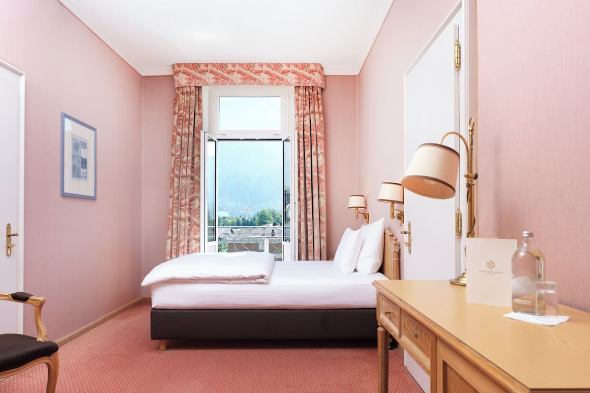 Ett hotellrum med en säng, ett skrivbord, en stol och utsikt över staden genom fönstret.