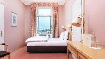 Quarto de hotel com cama, escrivaninha, cadeira e vista da cidade pela janela.