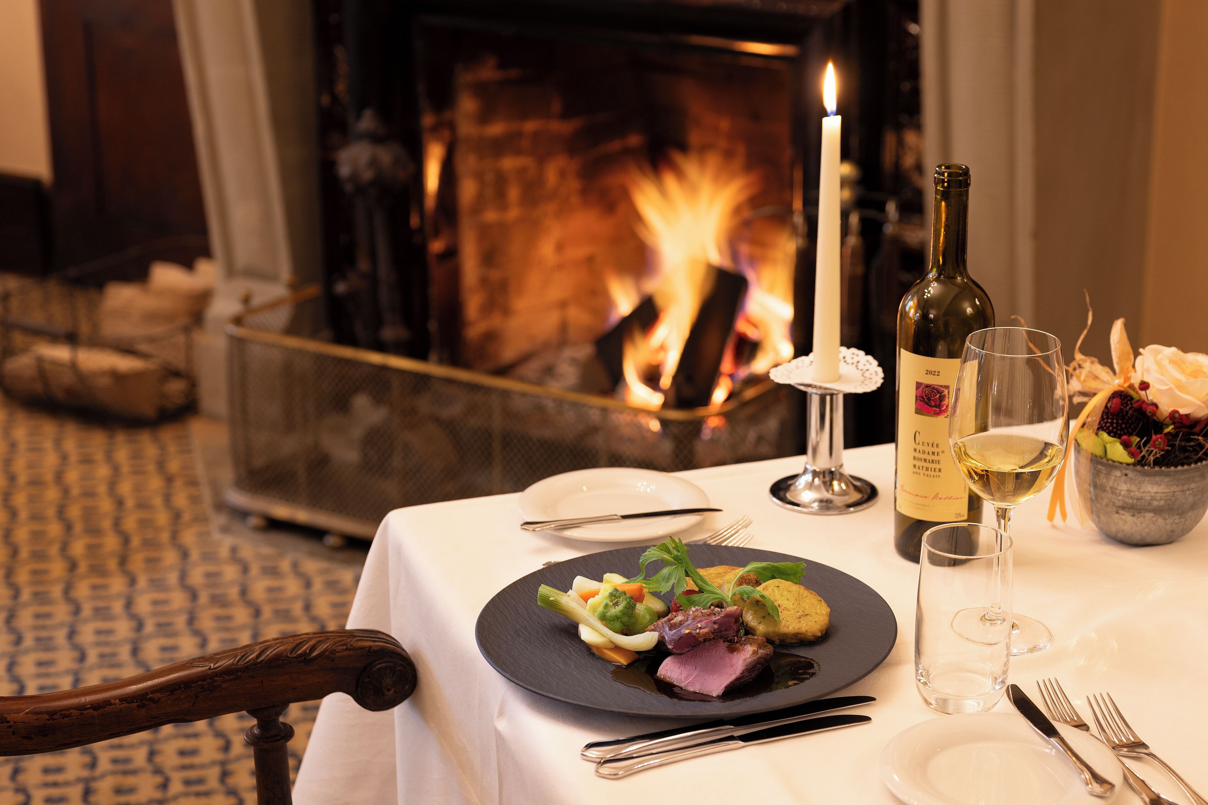 Une table à manger dressée avec une assiette de nourriture, une bouteille de vin et des verres.