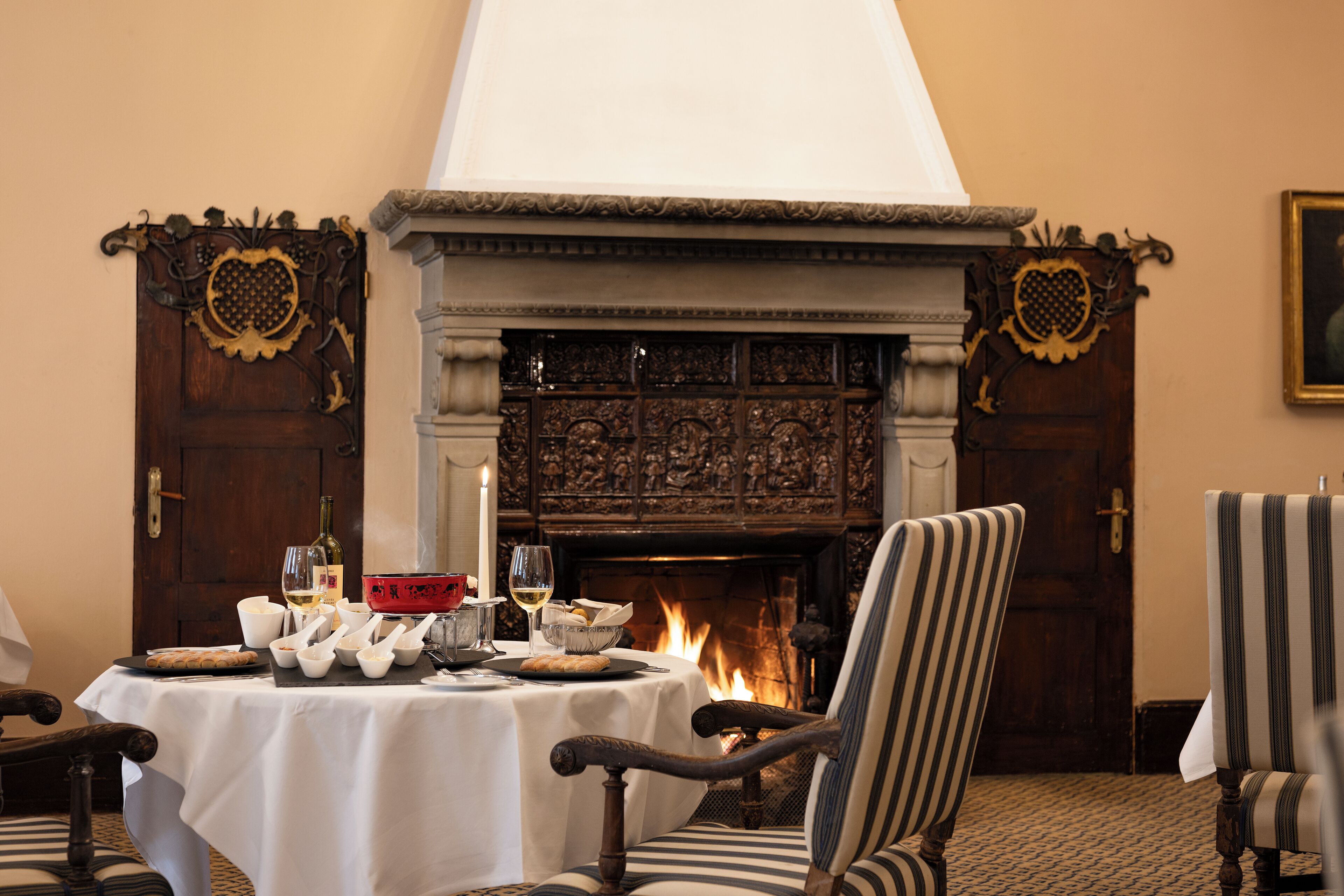 A dining area with a fireplace, table set with white tablecloth, and striped chairs.