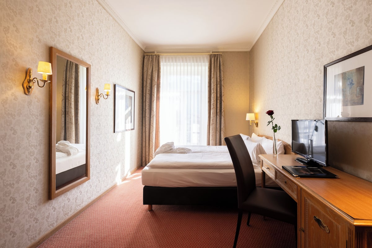 Ett hotellrum med en säng, ett skrivbord, en stol, en tv och en spegel.