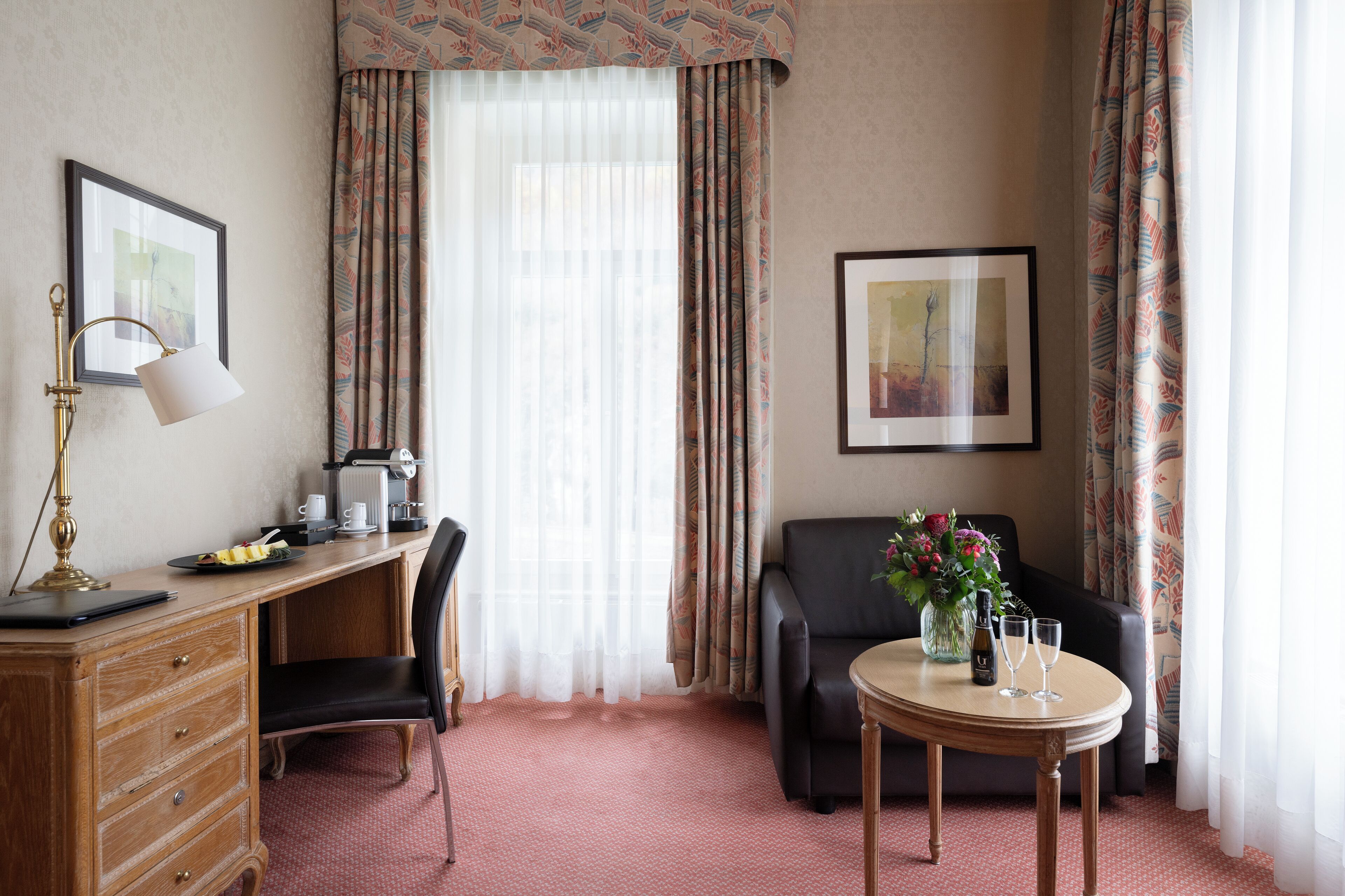 Habitación de hotel con escritorio, silla y una pequeña mesa con un florero y vasos.