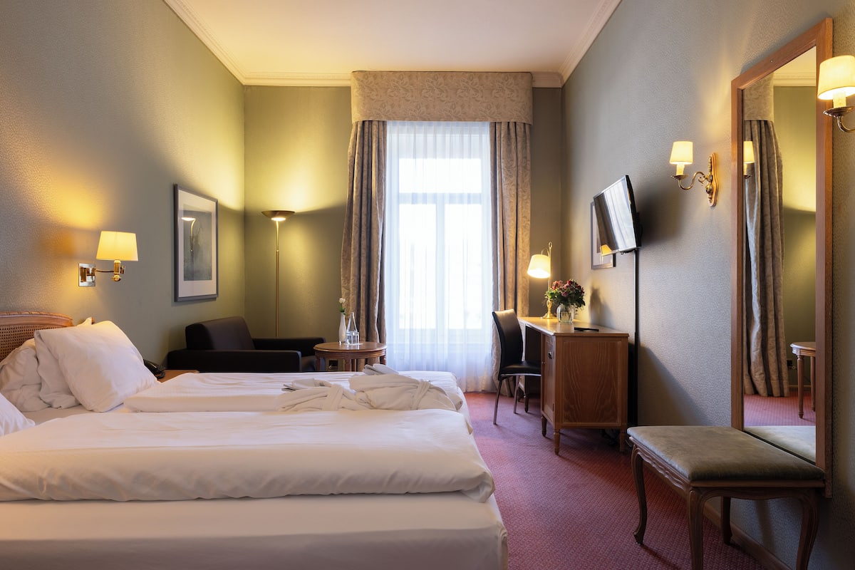 Ett hotellrum med en stor säng, ett skrivbord med en stol, en tv och en spegel.