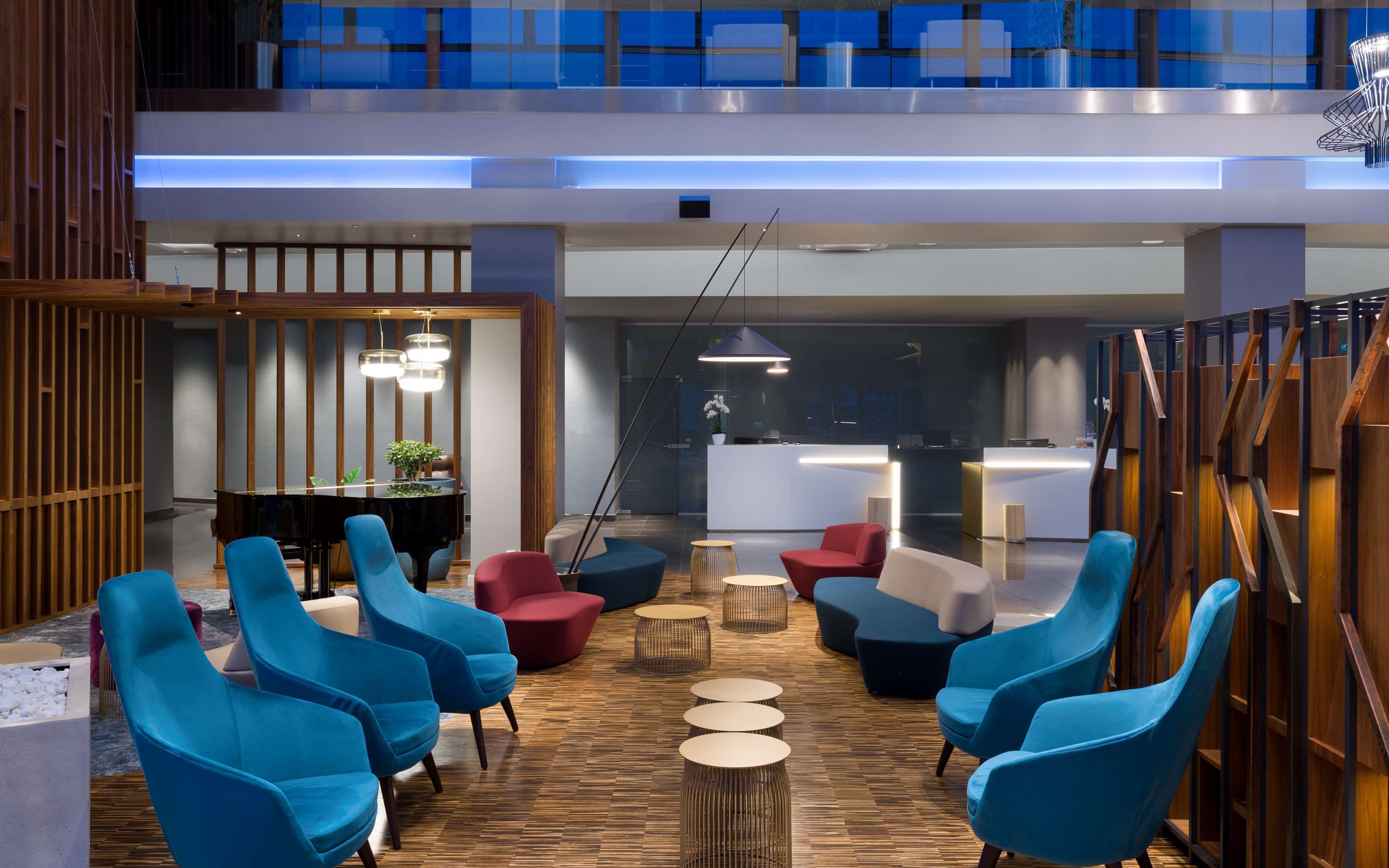 A modern lobby with blue and red chairs, a reception desk, and a wooden floor.