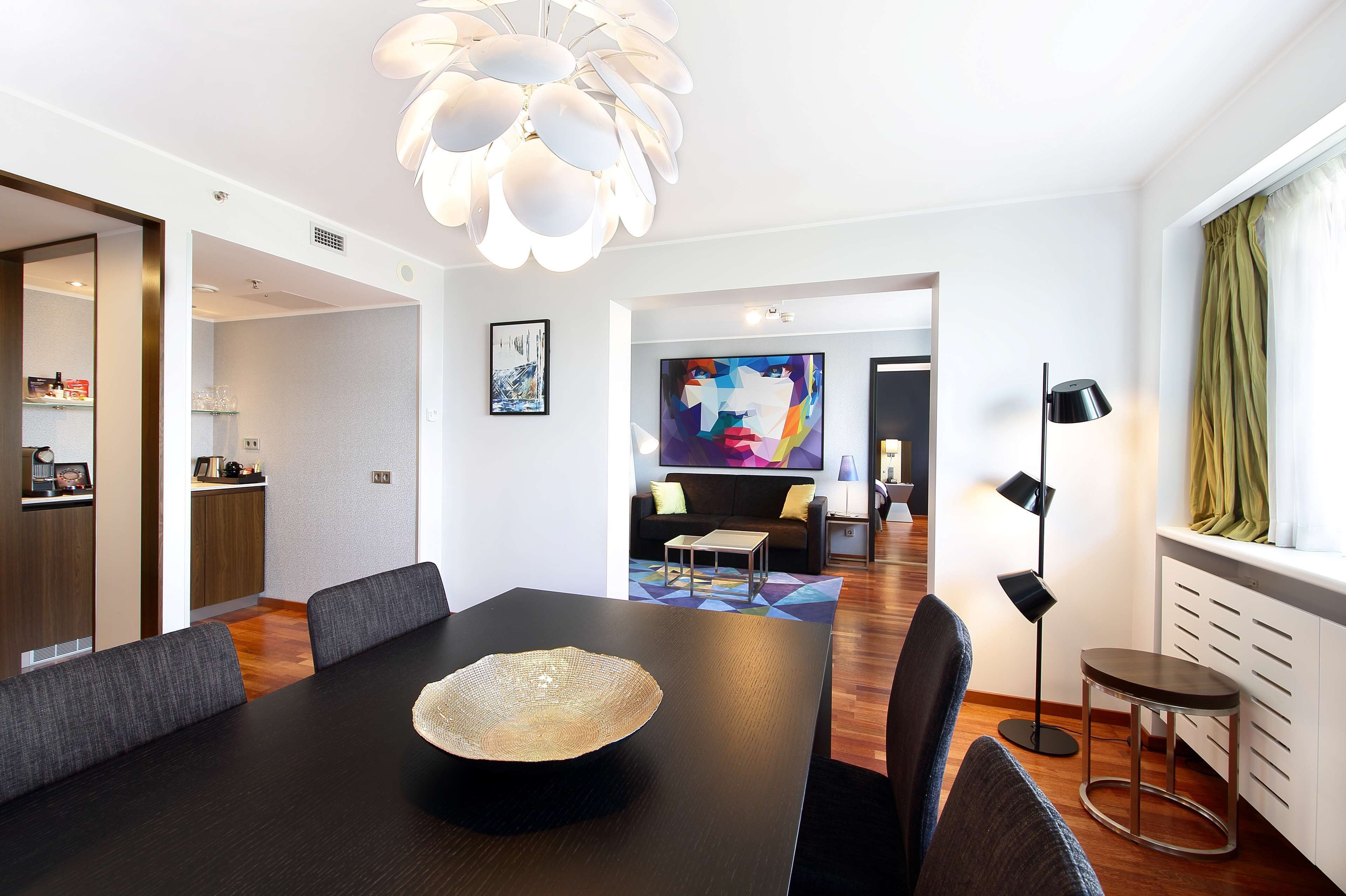 Un espace de salle à manger moderne, avec une grande table, des chaises rembourrées, un vase décoratif en guise de centre de table et un luminaire contemporain.