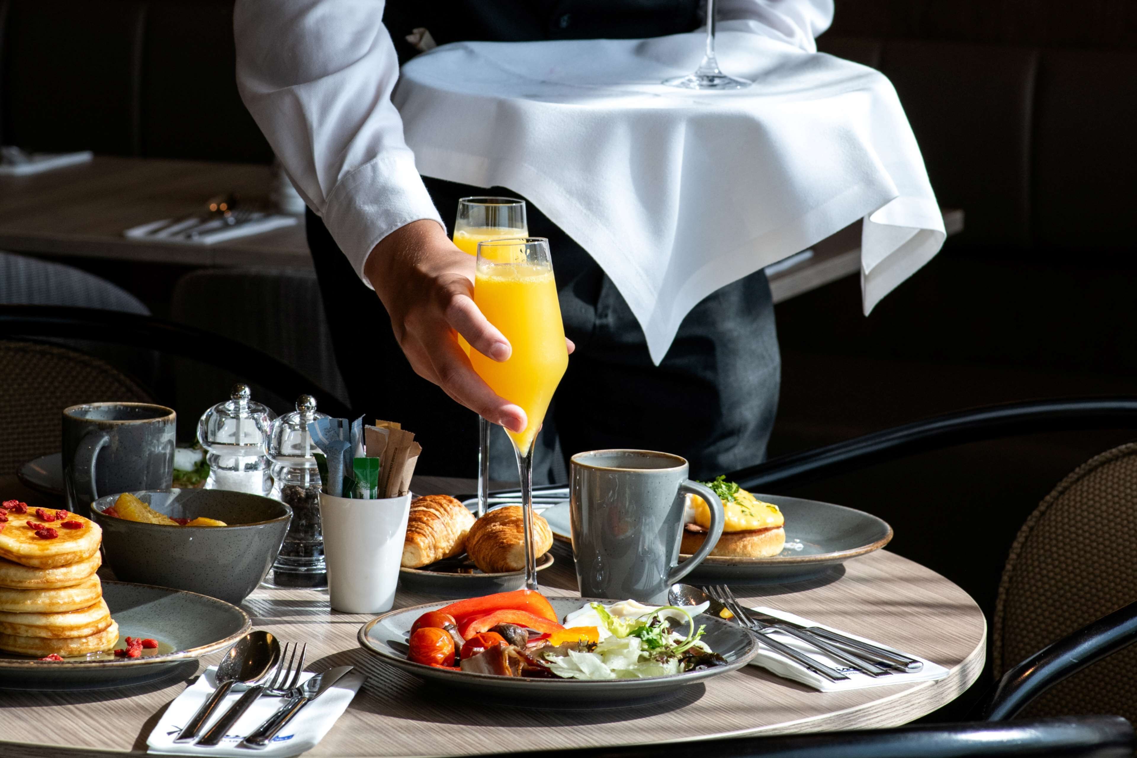 Una mesa con mantel blanco exhibe una variedad de platillos para el desayuno, como panqueques, croissants y verduras.