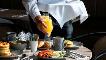Una mesa con mantel blanco exhibe una variedad de platillos para el desayuno, como panqueques, croissants y verduras.