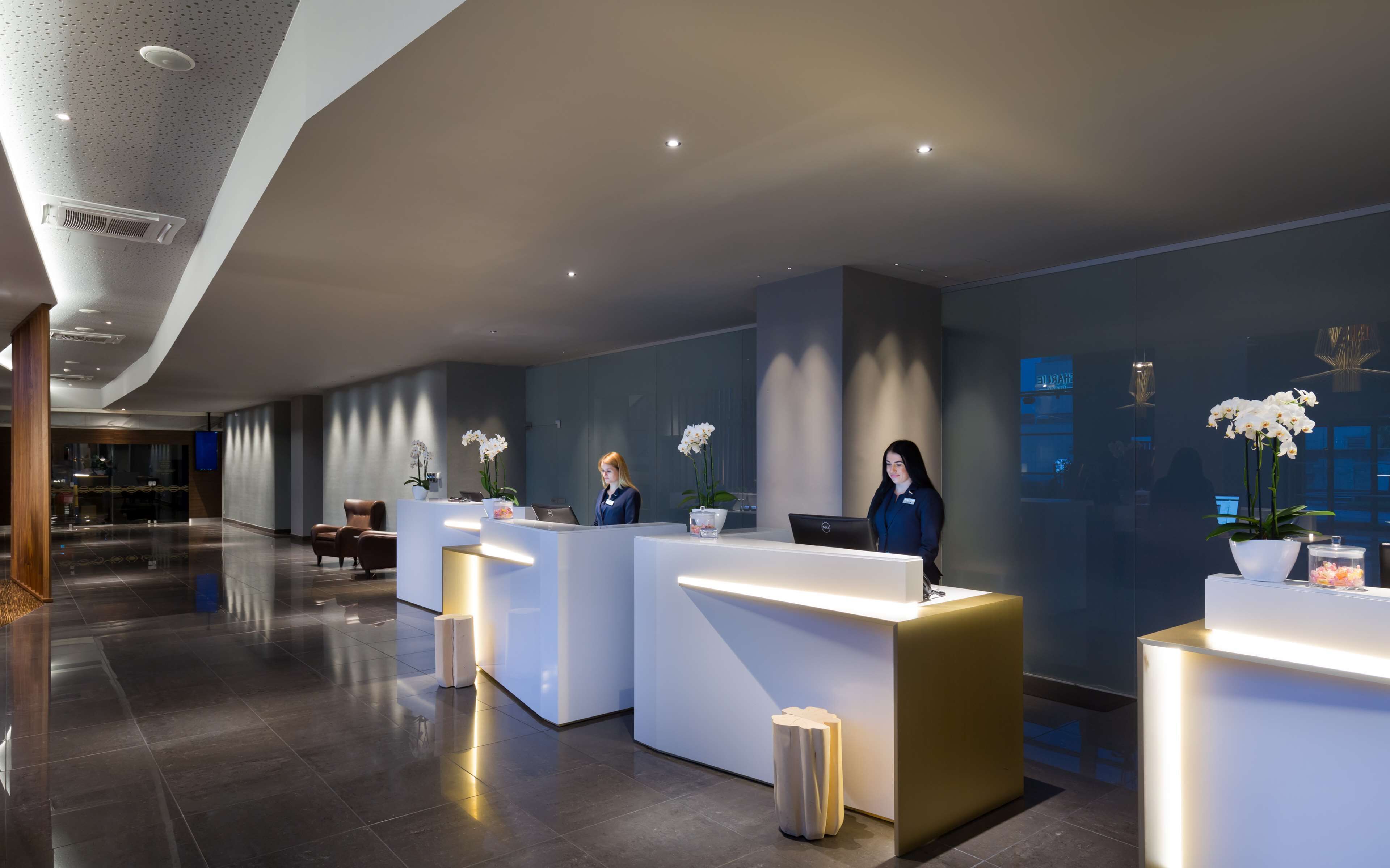 A modern hotel reception area with three reception desks, a large window, and a clean, polished floor.