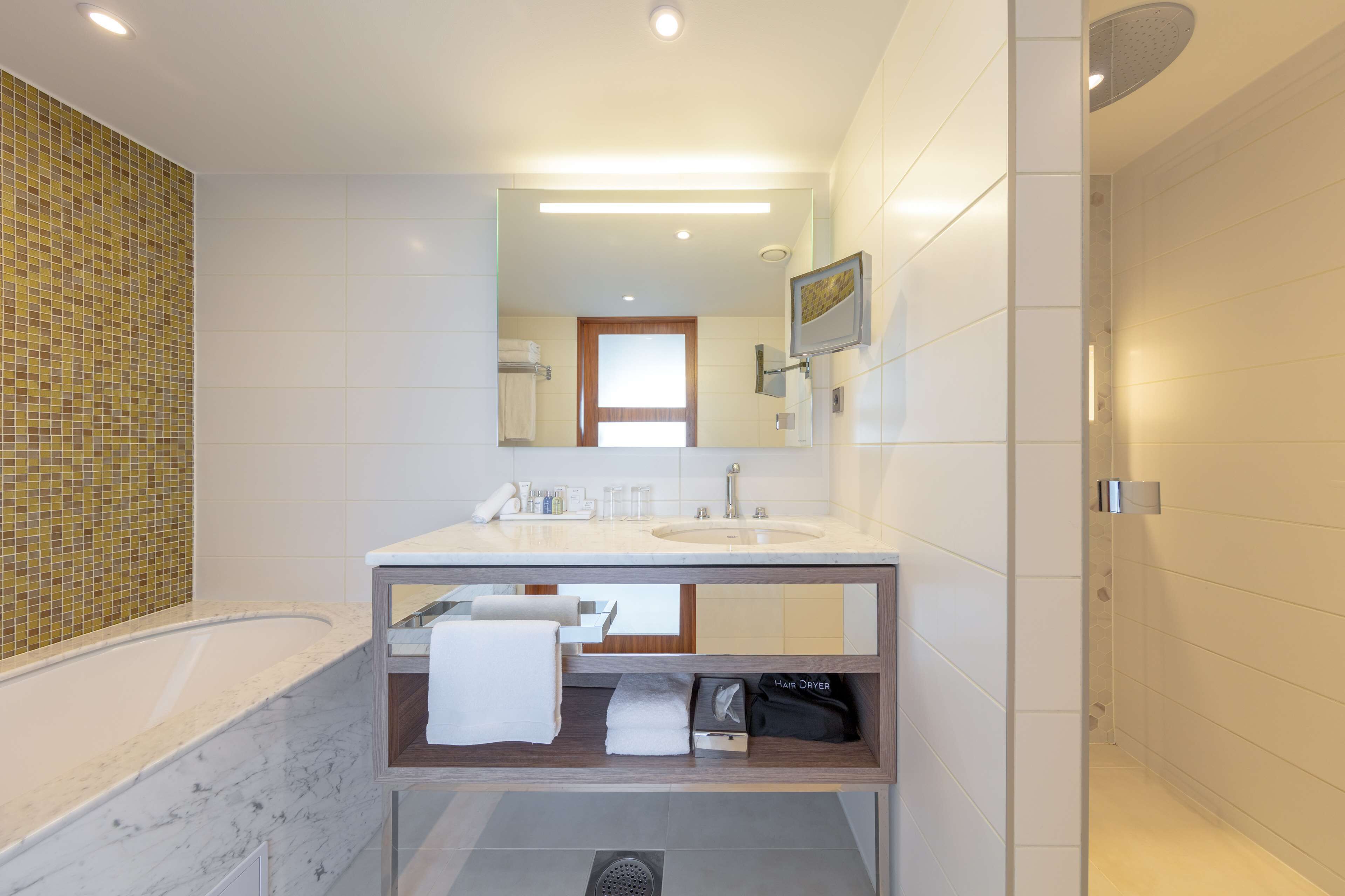 Ein modernes Badezimmer mit einem großen Spiegel, einem Waschbecken und einer Badewanne.