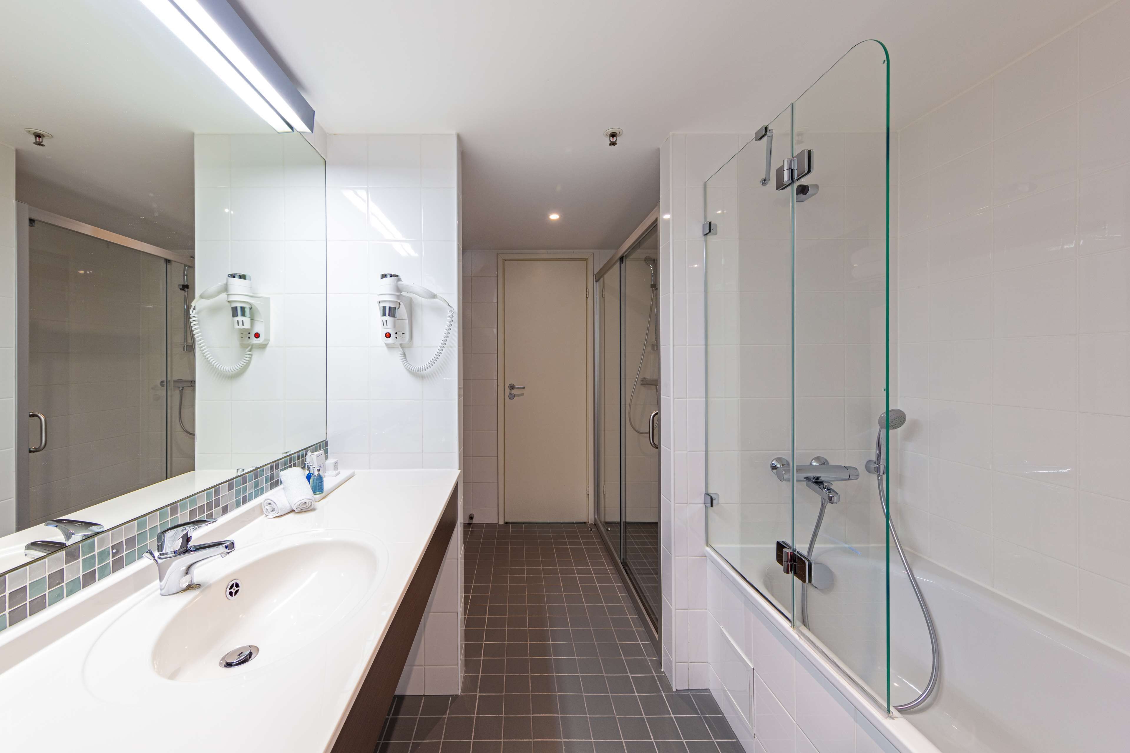 A modern bathroom with a large mirror, a white sink, a glass-enclosed shower, and a tiled floor.