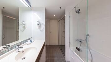 A modern bathroom with a large mirror, a white sink, a glass-enclosed shower, and a tiled floor.