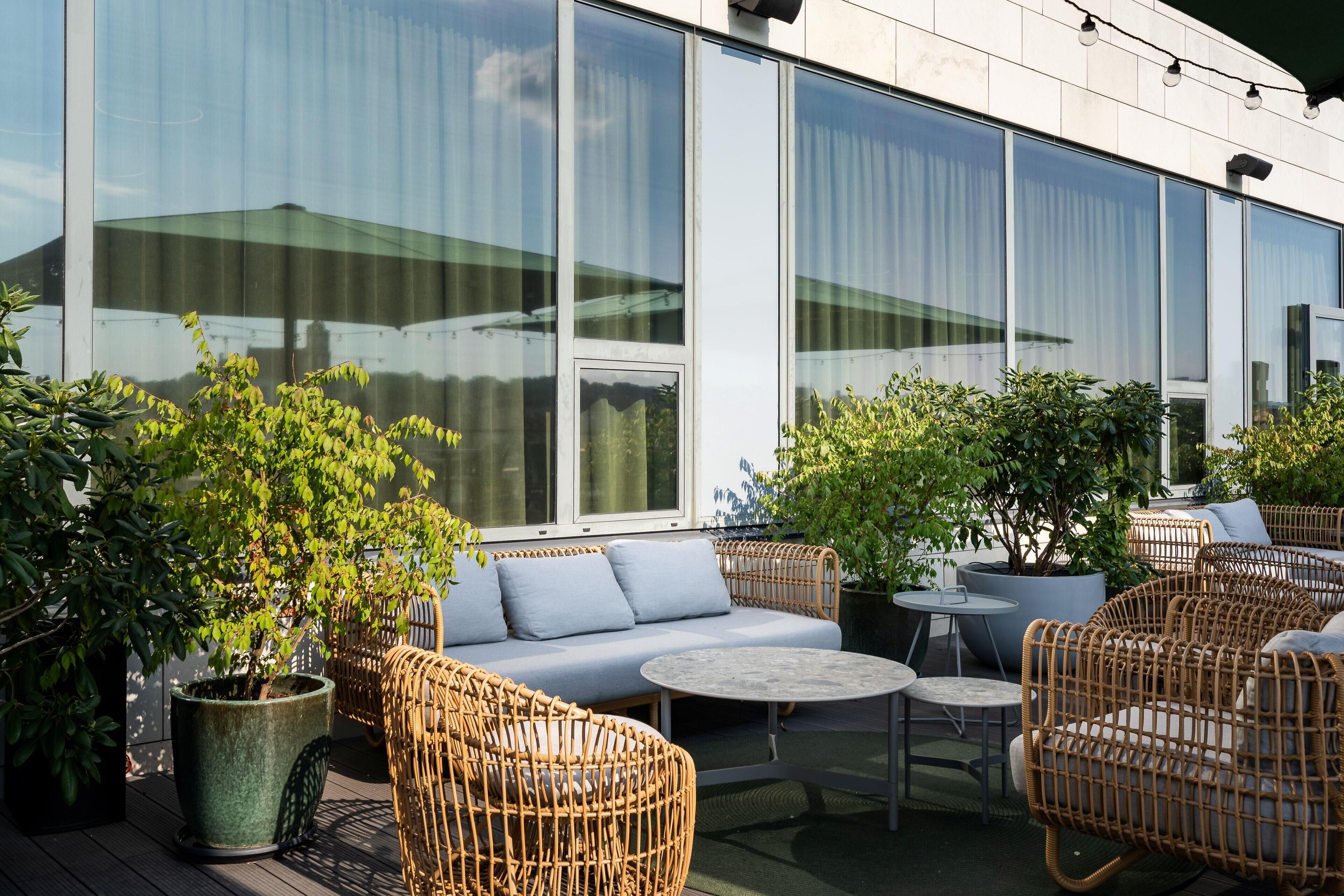 An outdoor seating area with wicker furniture, potted plants, and a view of a modern building with large windows.