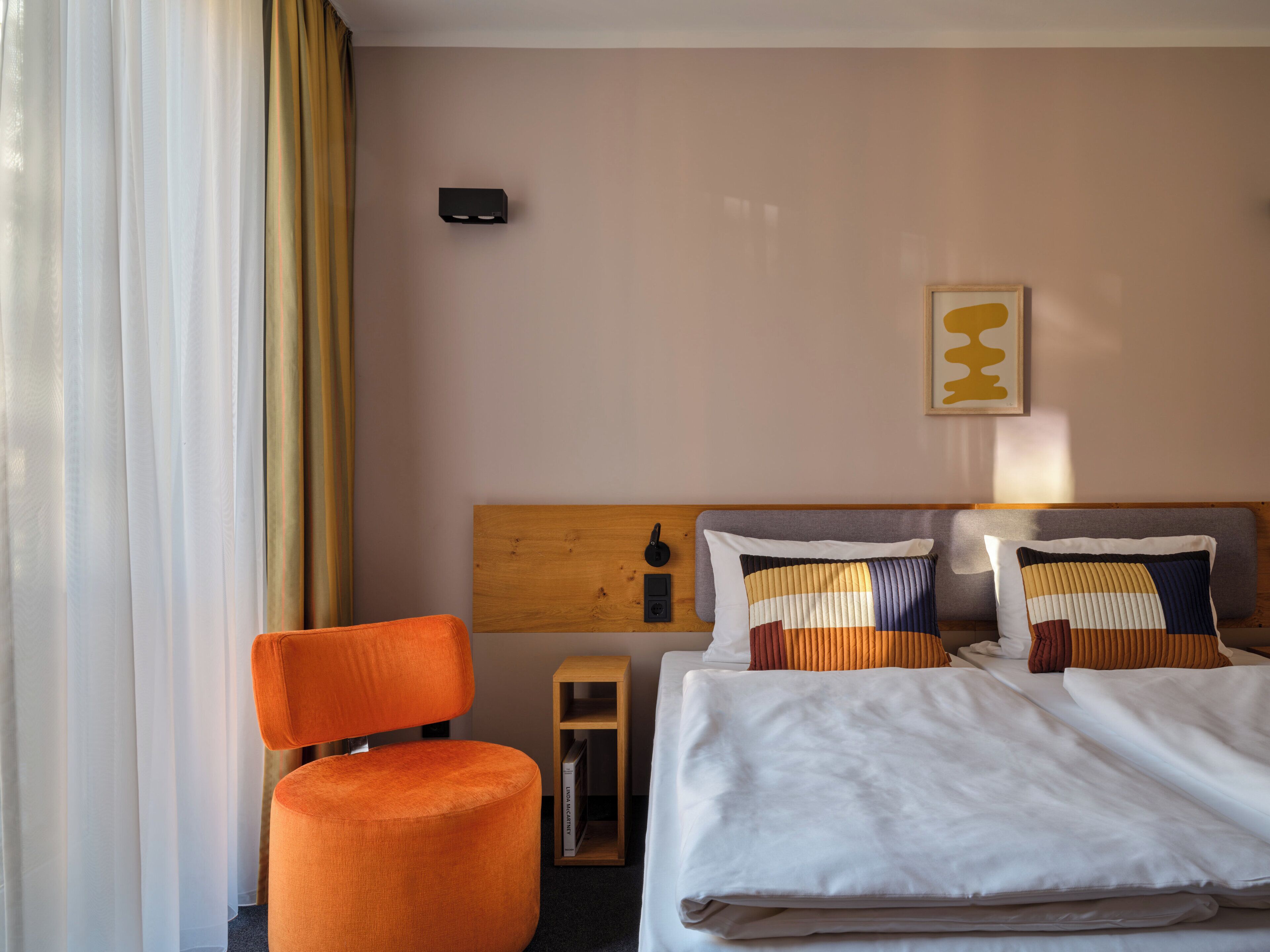 Ein Hotelzimmer mit einem Bett, einem orangefarbenen Sessel, einem Holz-Kopfteil und einer wandmontierten Klimaanlage.