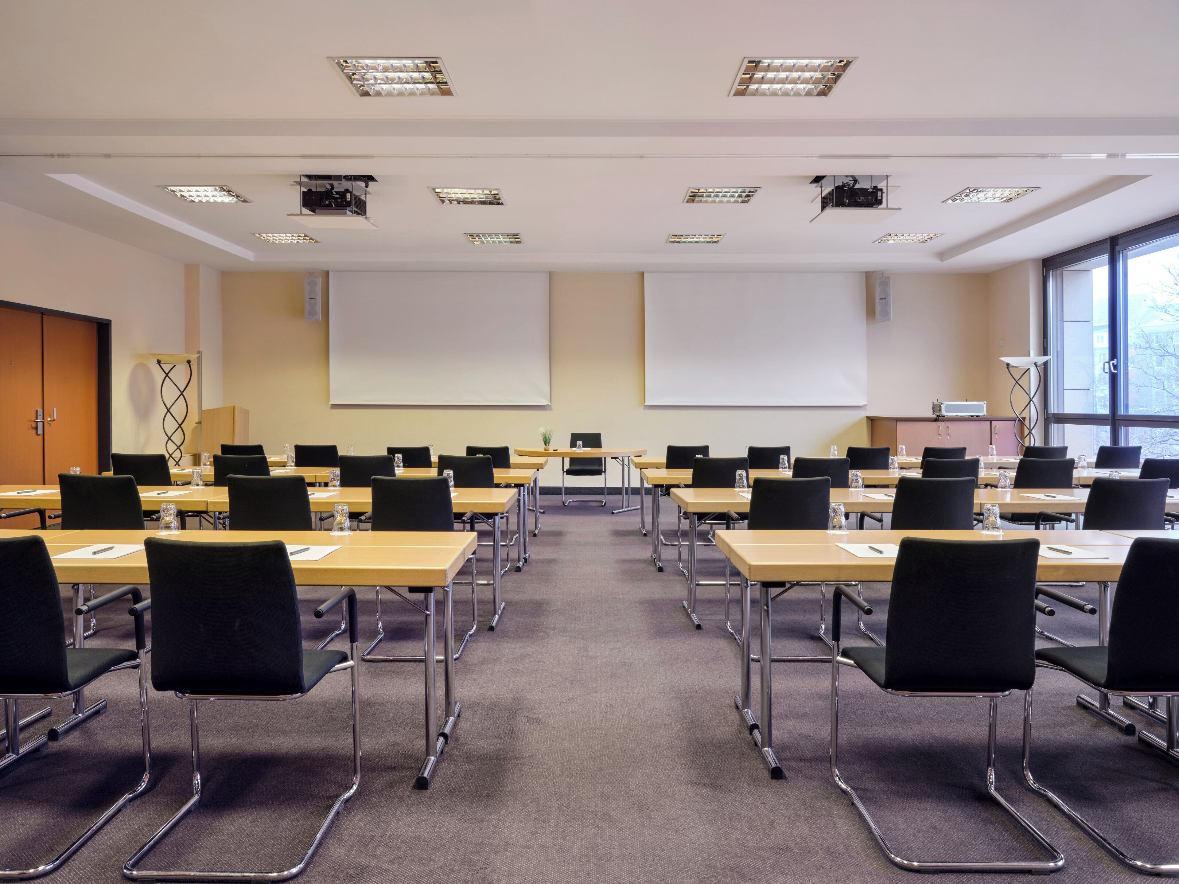 A conference room with rows of tables and chairs, a projector screen, and a large window.
