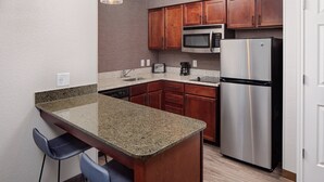 A compact kitchen with granite countertops, wooden cabinets, a stainless steel refrigerator, a microwave, and a dishwasher. - Residence Inn by Marriott Tucson Williams Centre (Tucson)