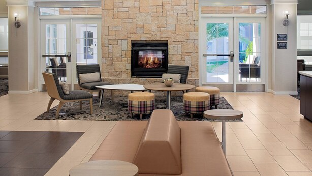 A modern lounge area with a stone fireplace, leather seating, and round tables. - Residence Inn by Marriott Tucson Williams Centre (Tucson)