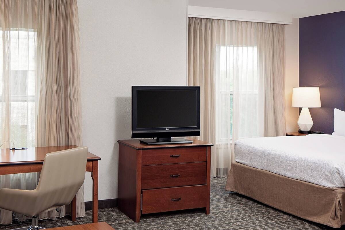 A hotel room with a bed, a desk with a chair, a television, and a lamp.