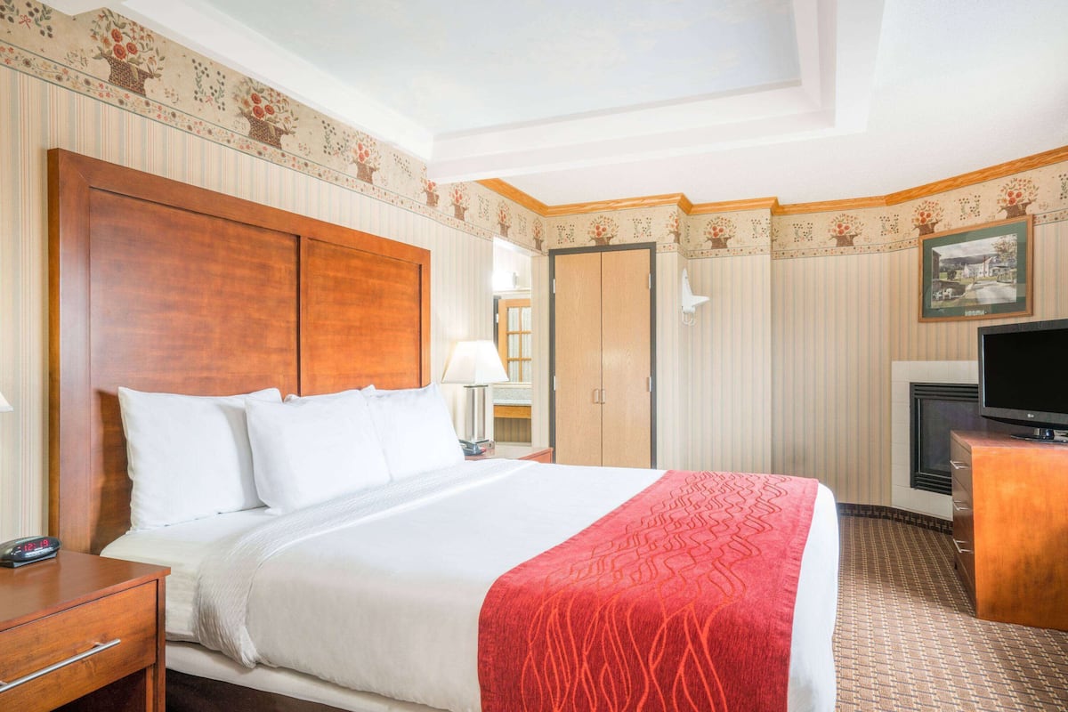 A hotel room with a large bed, a wooden headboard, a television, a desk, and a wardrobe.