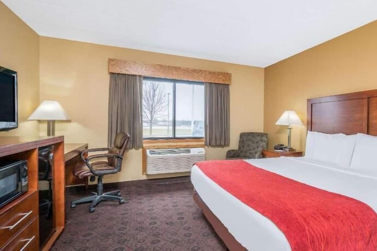 A hotel room with a bed, desk, chair, lamps, and a window with curtains.