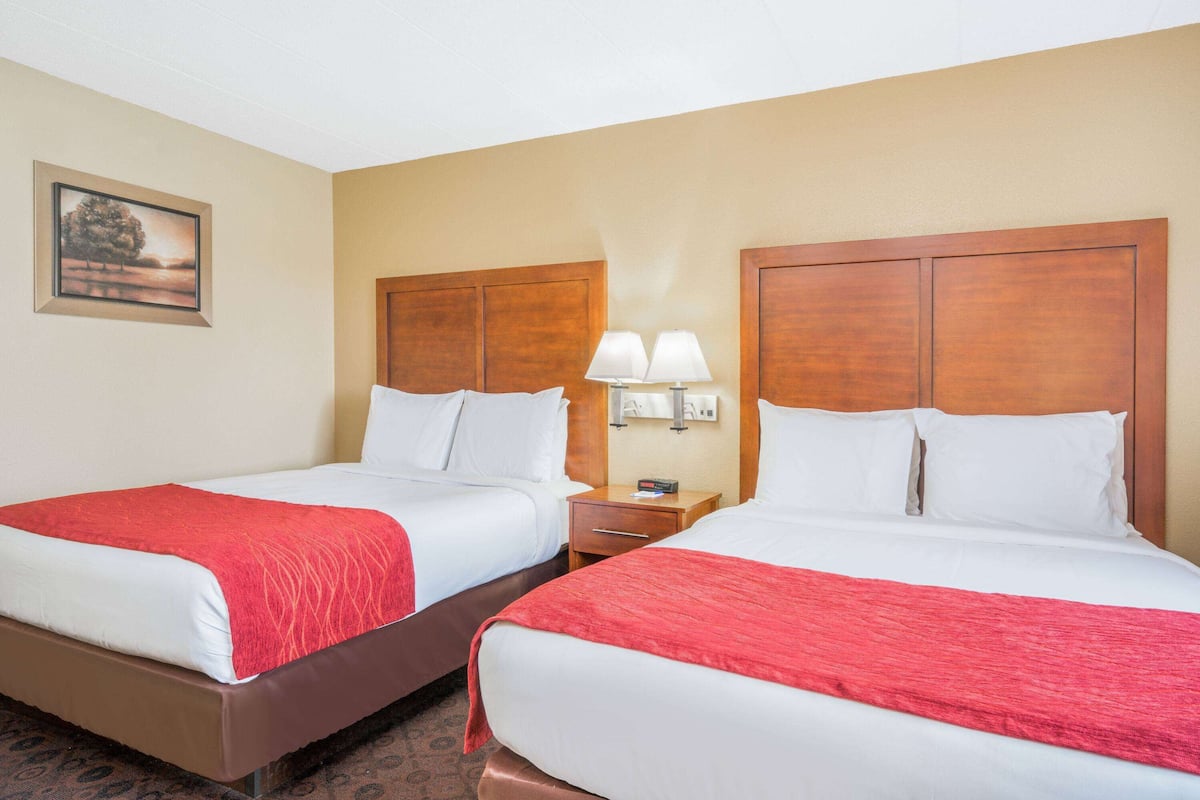 A hotel room with two beds, each with a red blanket, wooden headboards, and bedside lamps.