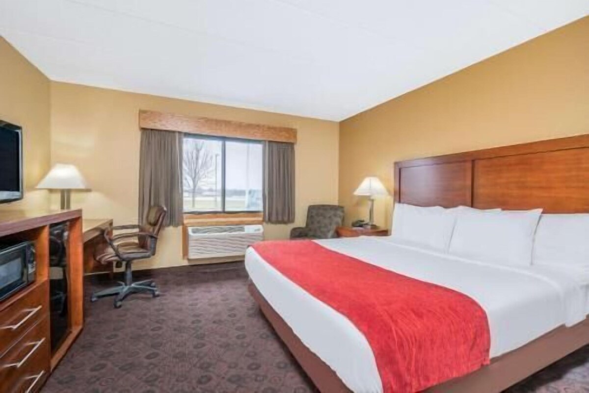 Ein Hotelzimmer mit einem Bett, zwei Stühlen, einem Schreibtisch, einem Fernseher und einem Fenster.