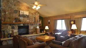 A living room with stone walls, a fireplace, leather furniture, and a ceiling fan. - Baymont by Wyndham Kasson Rochester Area (Kasson)