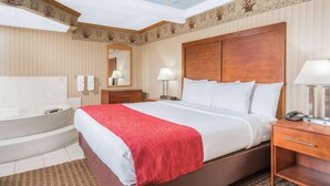 A hotel room with a large bed, a separate bathroom with a bathtub, and a skylight ceiling. - Baymont by Wyndham Kasson Rochester Area (Kasson)