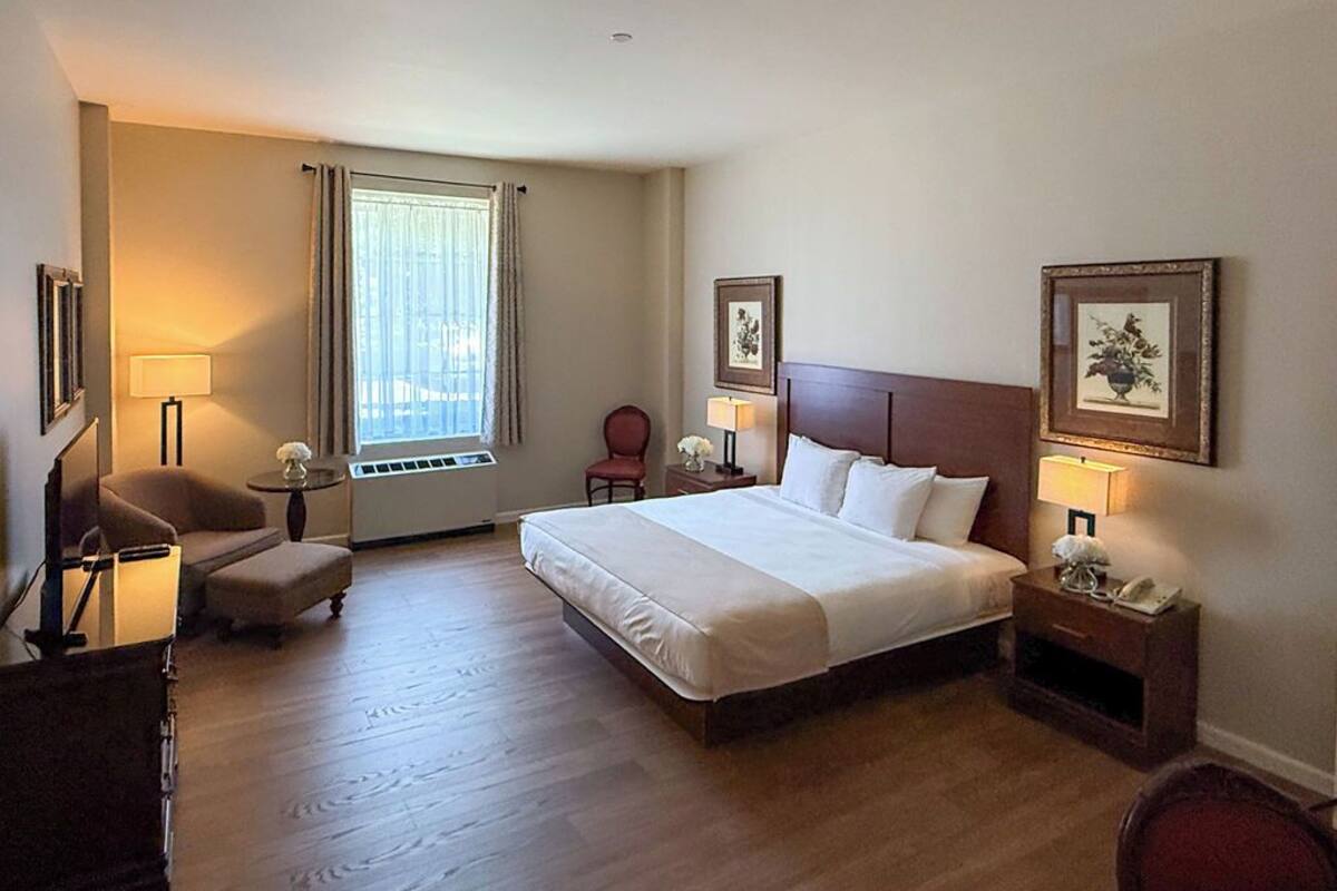 A hotel room with a large bed, a desk, a chair, a lamp, and a window with curtains.