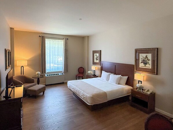 A hotel room with a large bed, a desk, a chair, a lamp, and a window with curtains.
