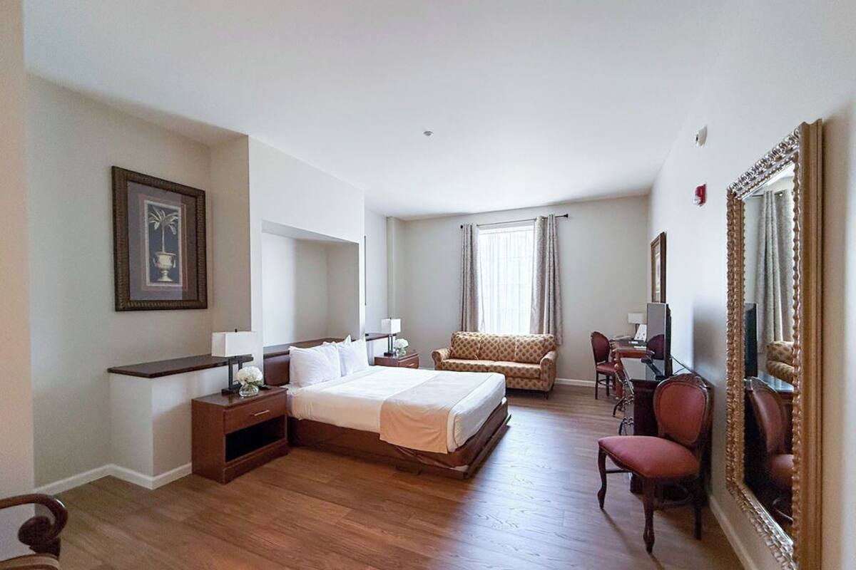 A hotel room with a large bed, a desk, a chair, a sofa, and a mirror.