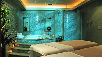 A spa room with a large bathtub, two beds, and a mirror.