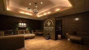 Interior d'un spa i saló de bellesa amb sòls de fusta, sofàs beigs i una estàtua de Buda.