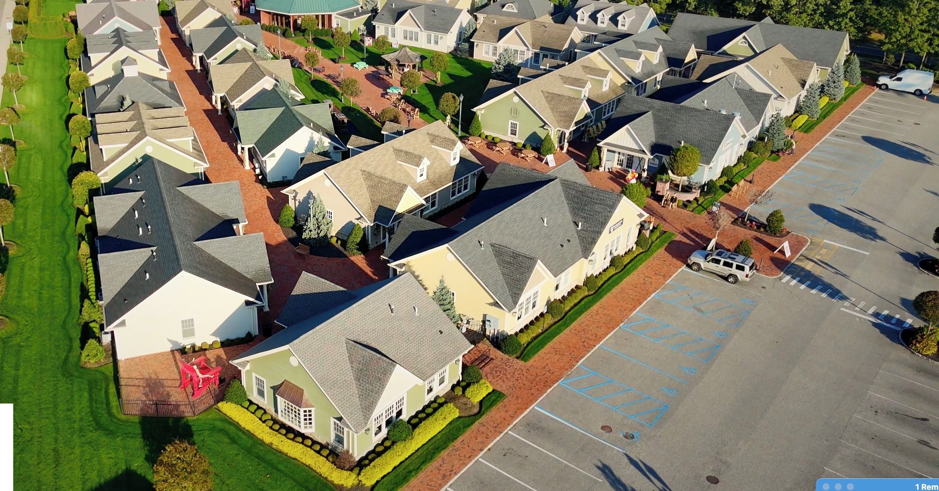 An aerial view of a residential area with houses, a parking lot, and a green space.