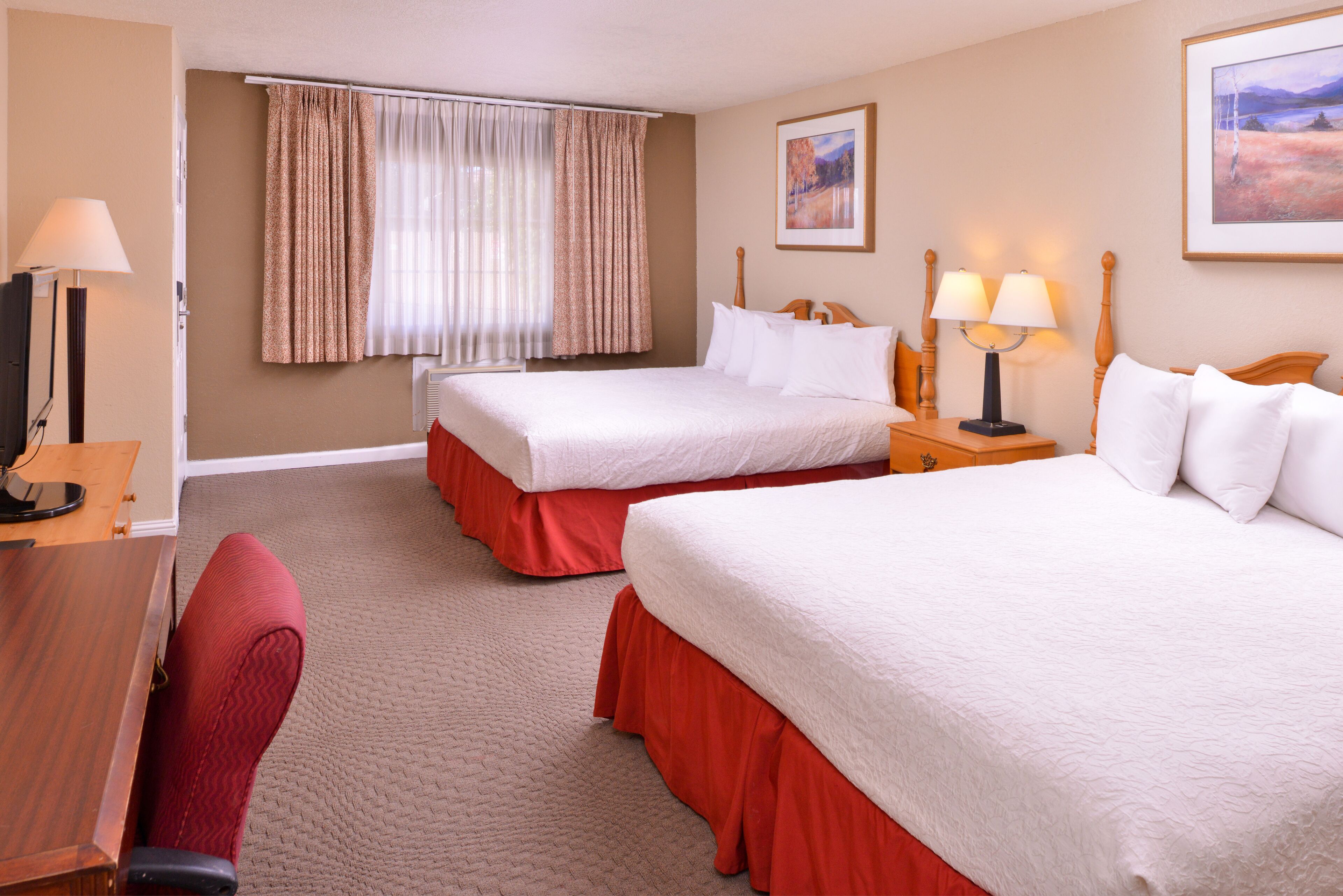 A hotel room with two beds, a desk, a chair, a TV, and a window with curtains.