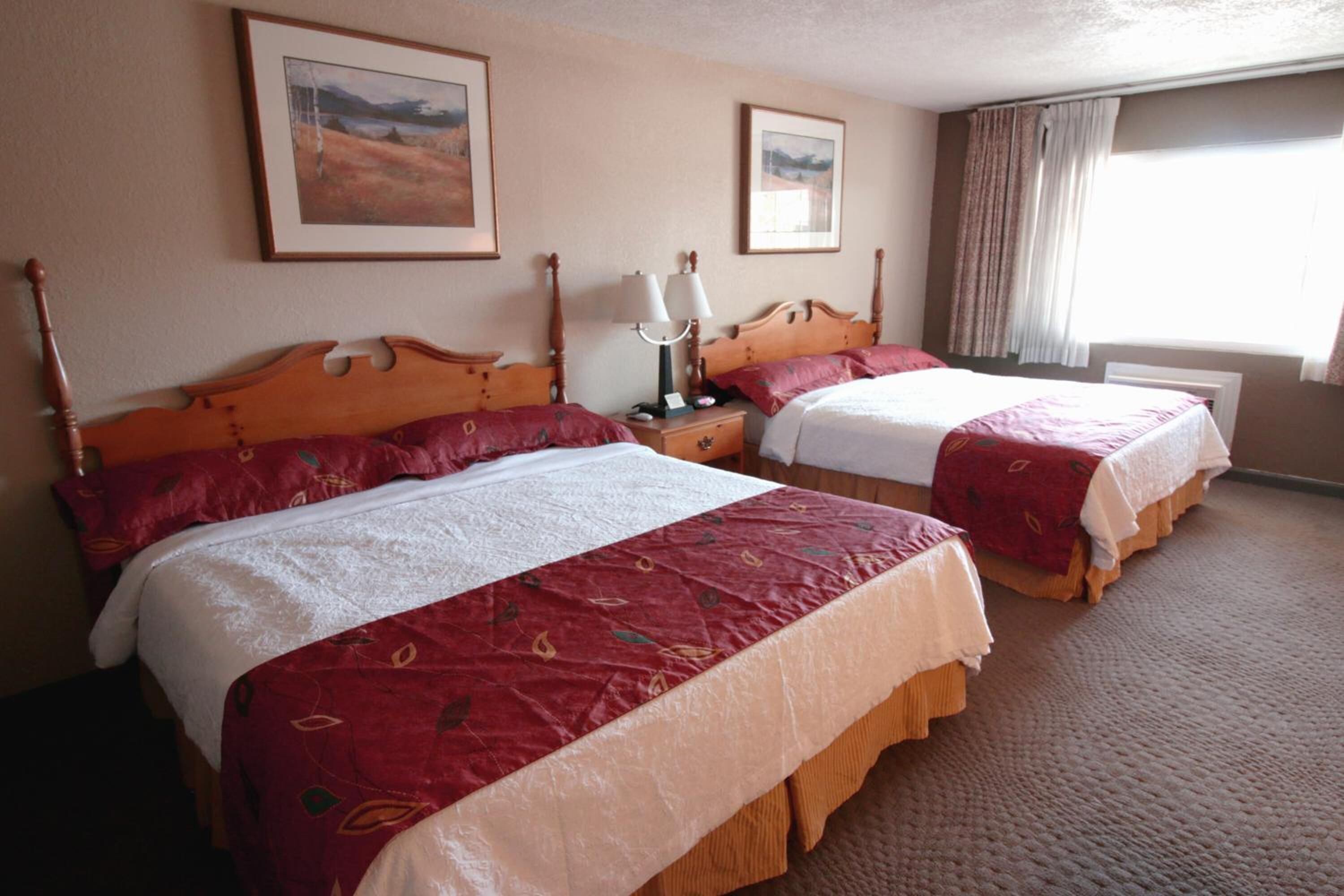 A hotel room with two beds, each with a wooden headboard, a nightstand with a lamp, and framed pictures on the wall.