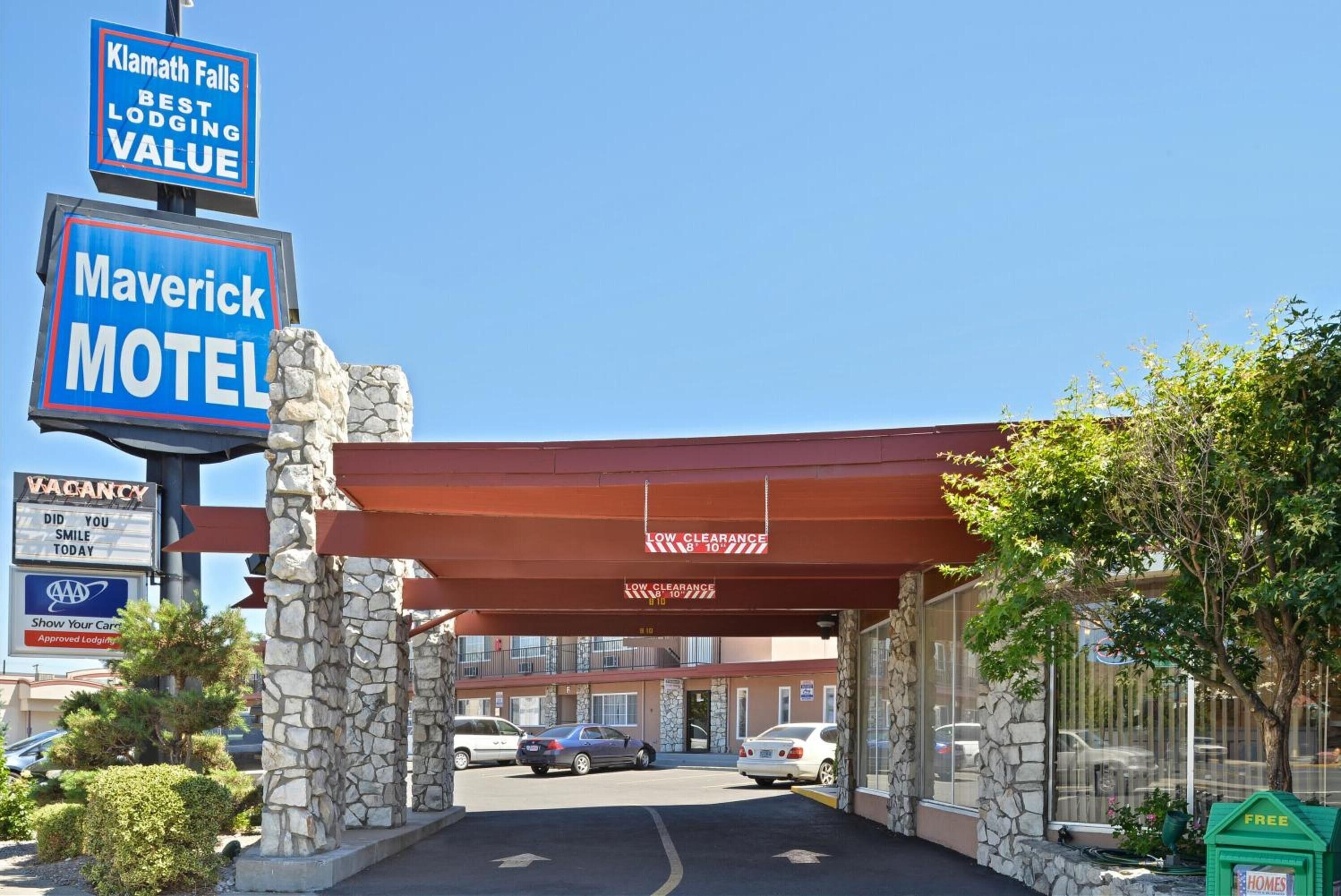 A motel with a stone facade, a red awning, and multiple signs including 'Maverick Motel' and 'Klamath Falls Best Lodging Value'.
