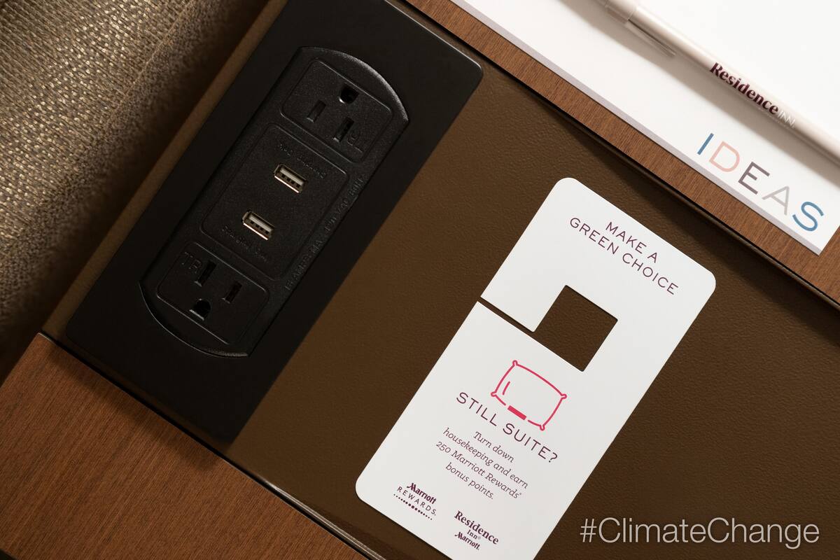 A hotel room with a brown wooden floor, a black power strip, and a white card with text.