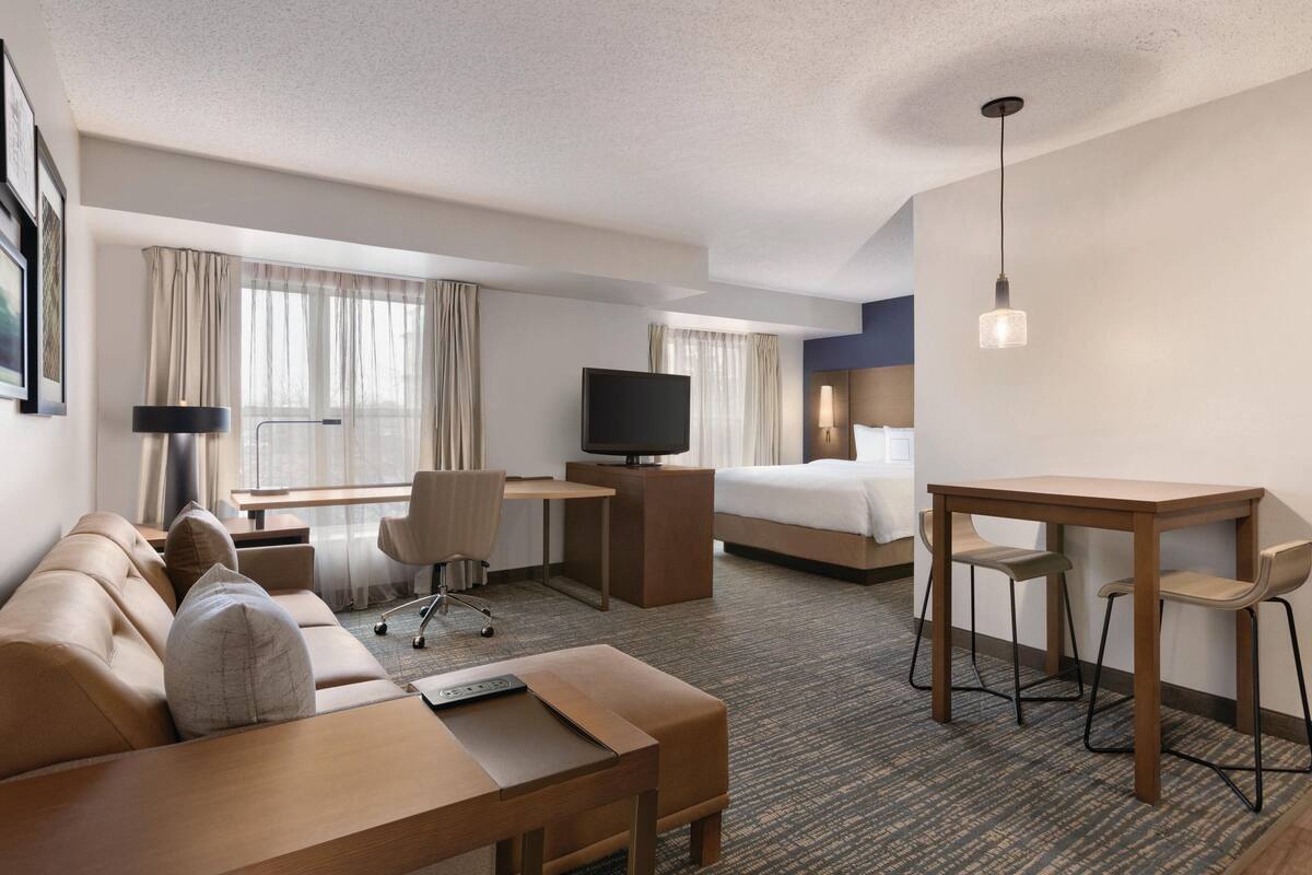 A hotel room with a sofa, desk, TV, and a bed.