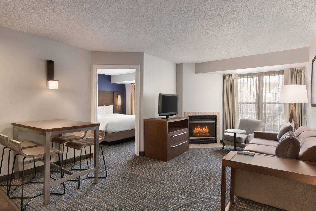 A hotel room with a bed, a TV, a fireplace, a sofa, a desk, and chairs.