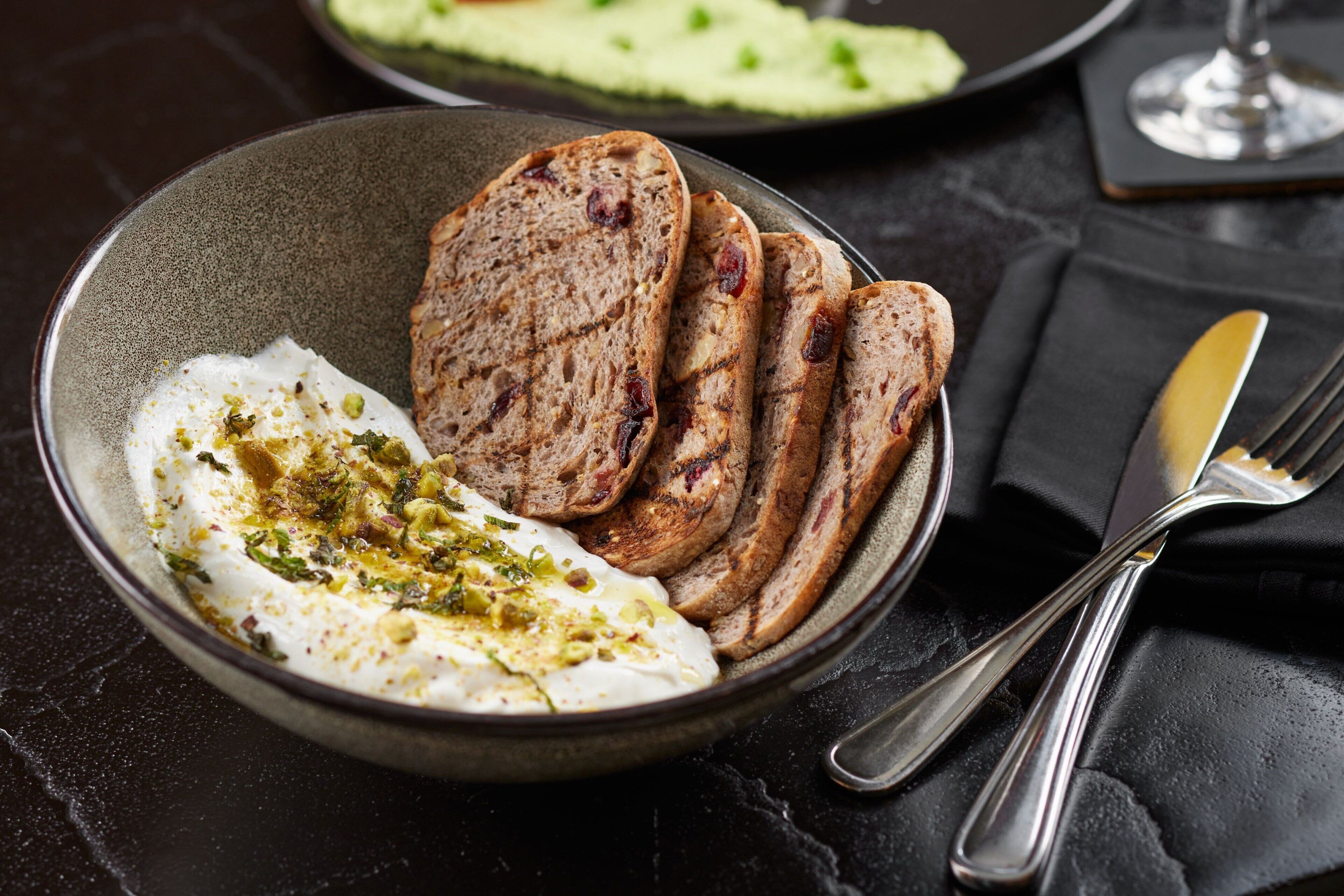 A bowl of food with bread and a creamy white sauce, accompanied by a fork and knife on a dark surface.