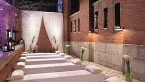 A spa area with multiple treatment beds aligned along a brick wall, each with a white cushion and surrounded by white flowers. - The Ritz-Carlton Georgetown, Washington, D.C. (Washington)