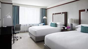Habitación de hotel con dos camas, un escritorio, una silla, una lámpara y una ventana con cortinas.