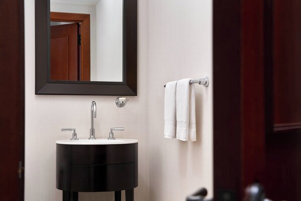 A bathroom with a round black sink, a mirror, and a towel rack with two white towels.