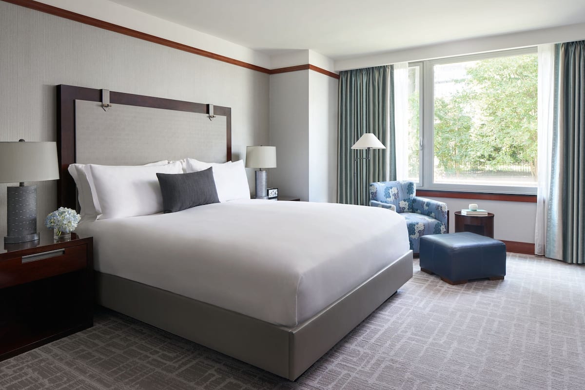 A hotel room with a large bed, bedside tables, a chair, a small table, and a window with curtains.