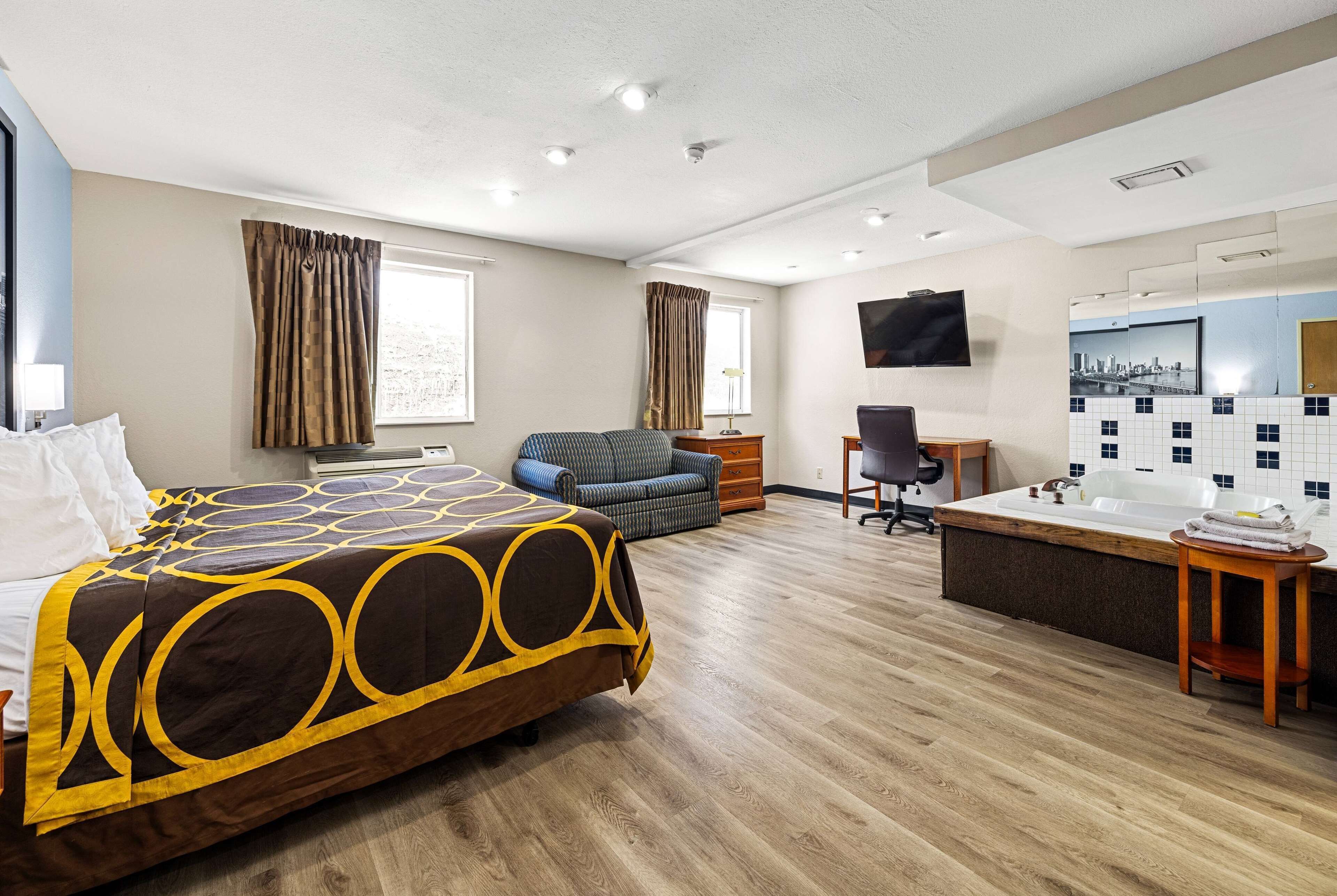 A hotel room with a bed, a desk, a chair, a sofa, a bathtub, and a TV.