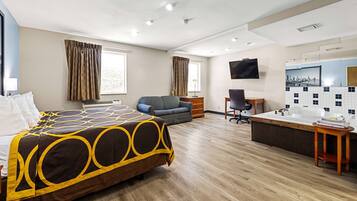 A hotel room with a bed, a desk, a chair, a sofa, a bathtub, and a TV.