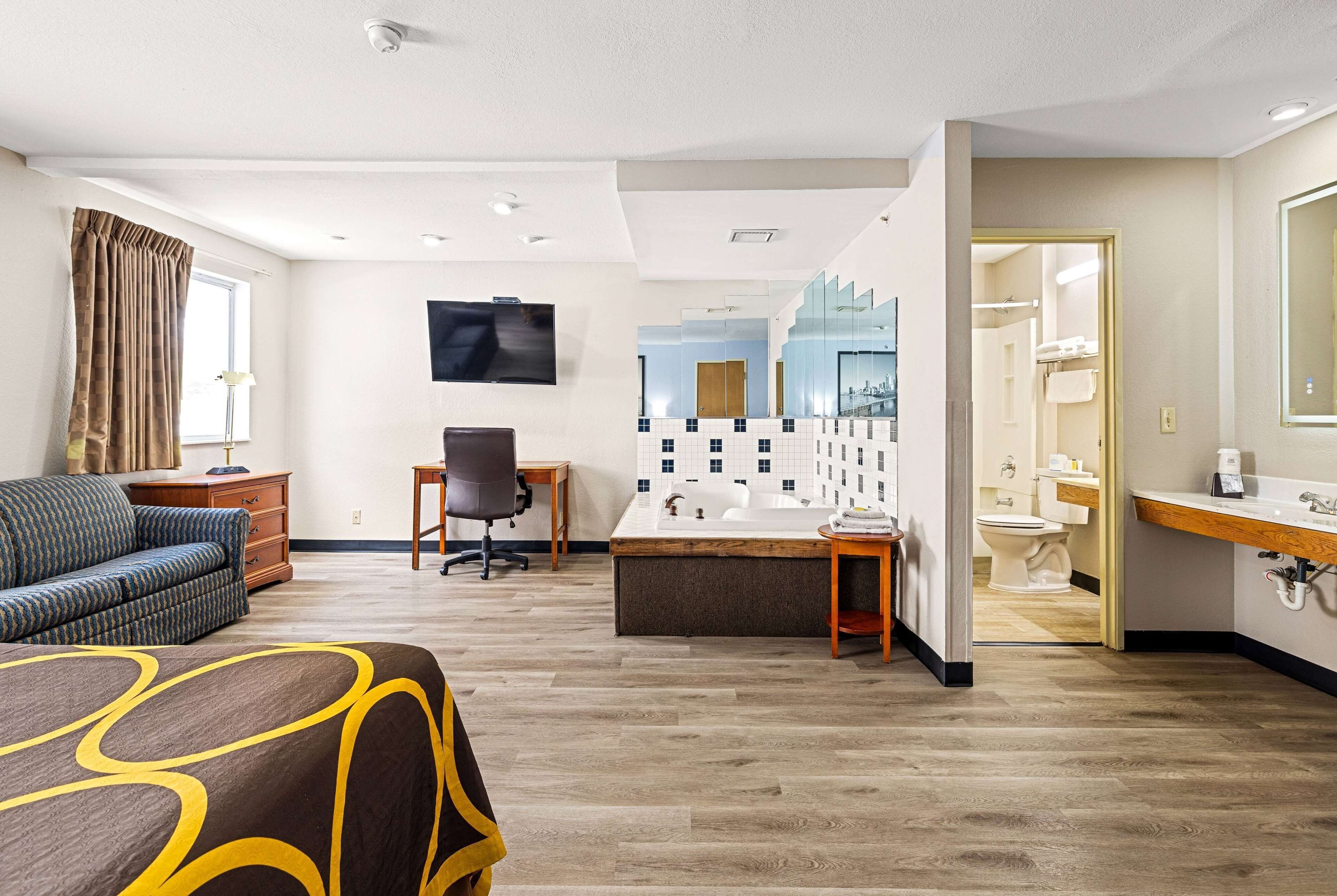 A hotel room with a bed, a desk, a chair, a TV, a bathroom with a sink and toilet, and a mirror.