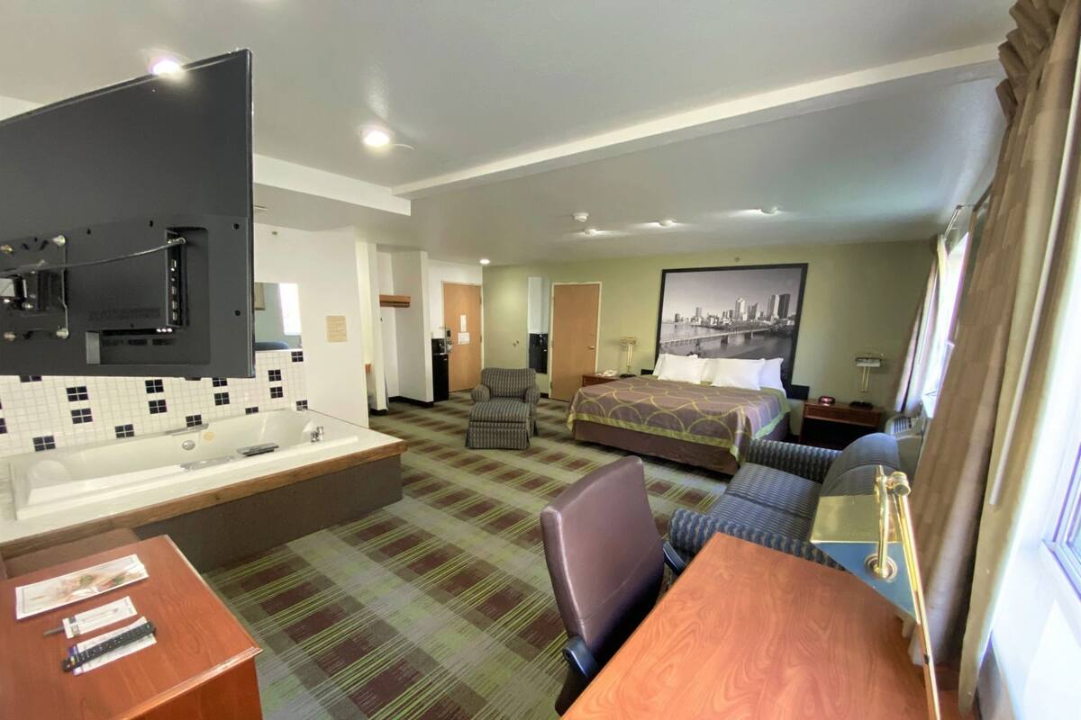 A hotel room with a bed, a desk with a chair, a bathroom with a sink, and a large window.