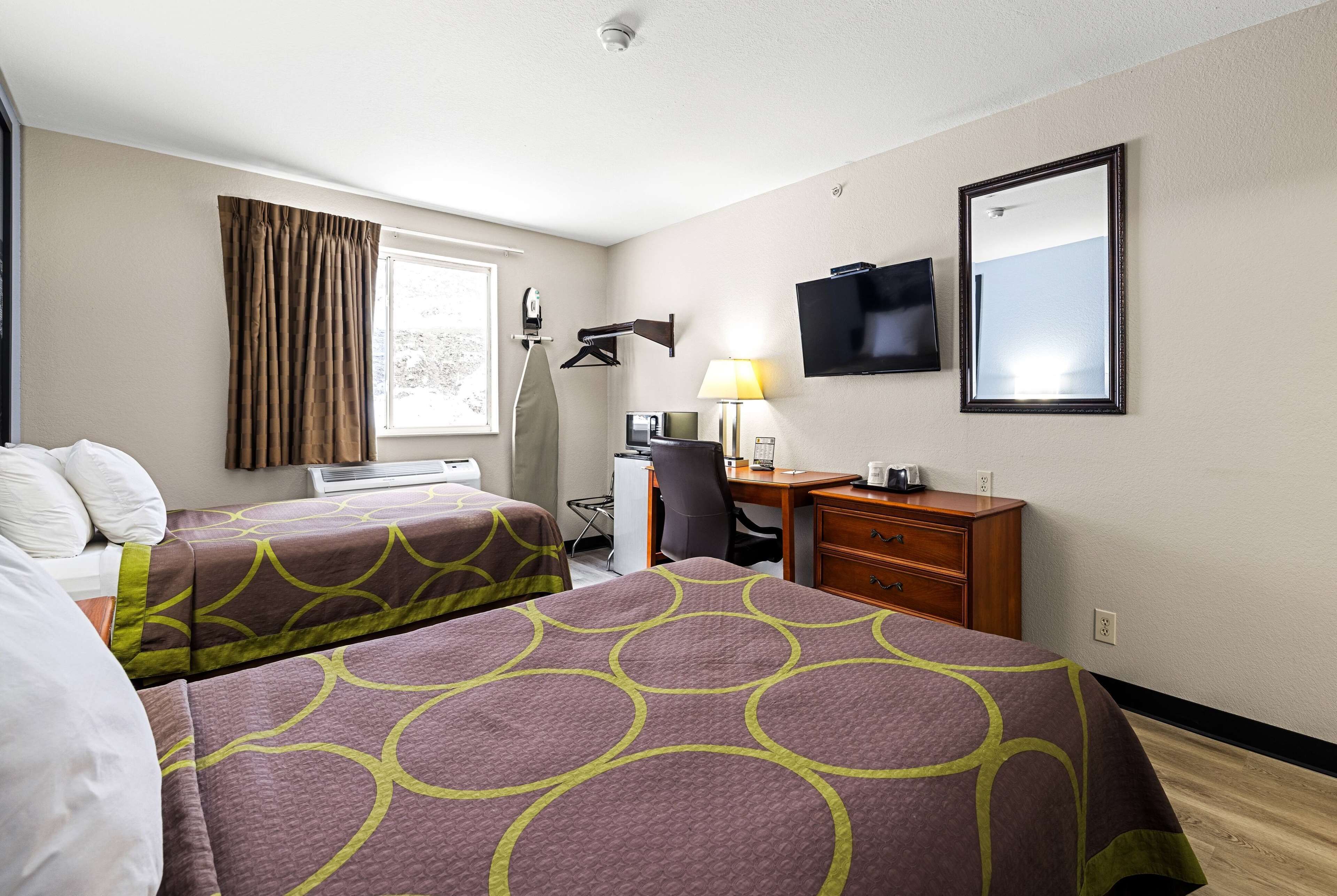 A hotel room with two beds, a desk, a chair, a TV, and a window with curtains.